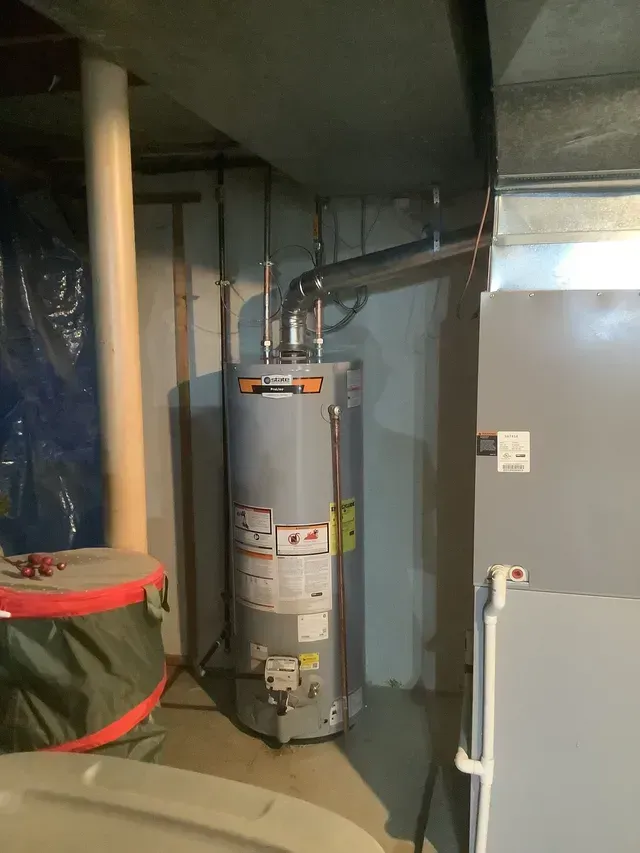 A furnace is sitting in the corner of a room next to a door.