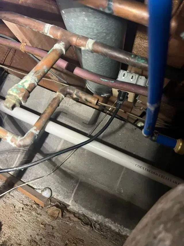 A bunch of pipes are hanging from the ceiling in a basement.