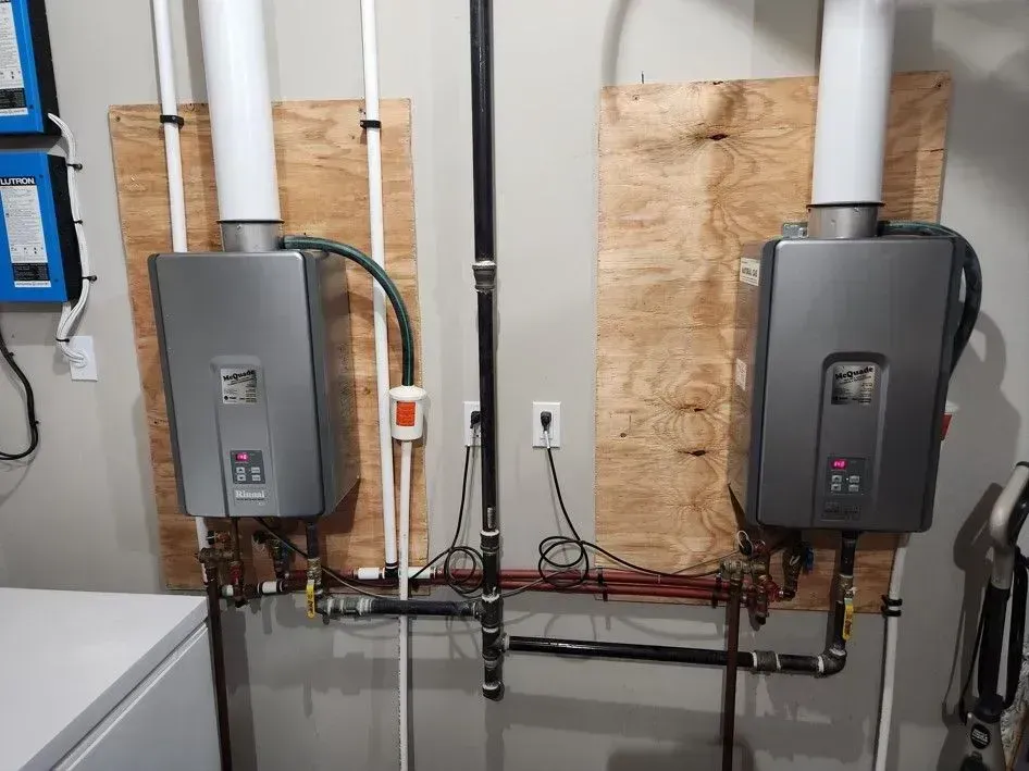 Two water heaters are hanging on the wall in a laundry room.