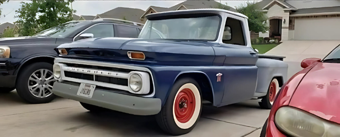 A blue truck is parked next to a red car in a driveway.