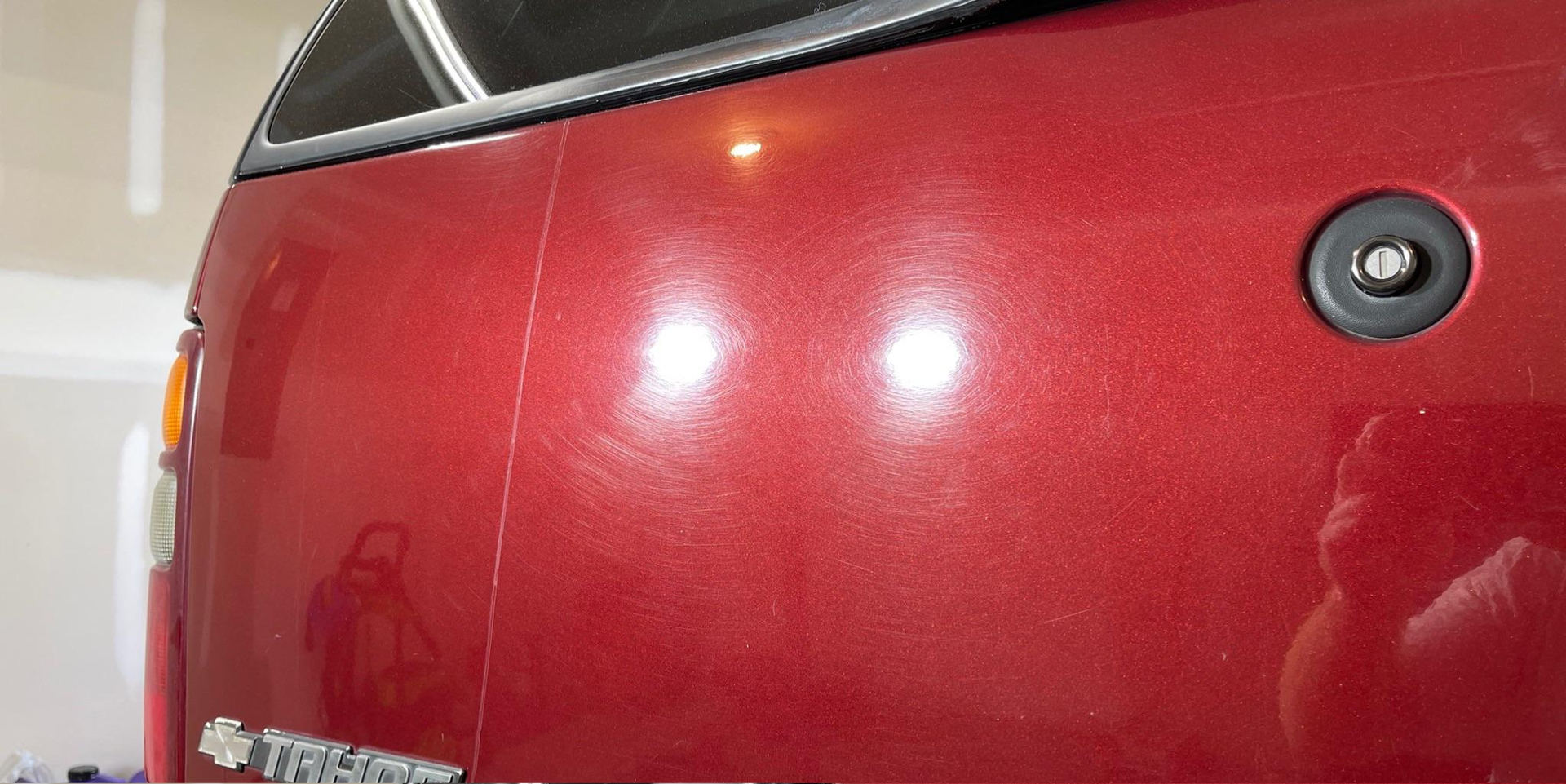 A red truck is parked in a garage with a person taking a picture of it.