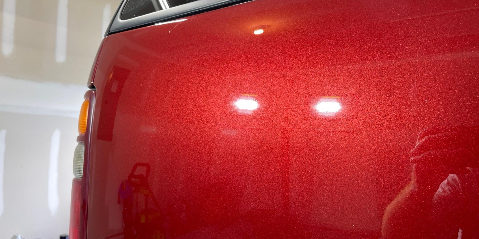A red truck is parked in a garage and a person is taking a picture of it.