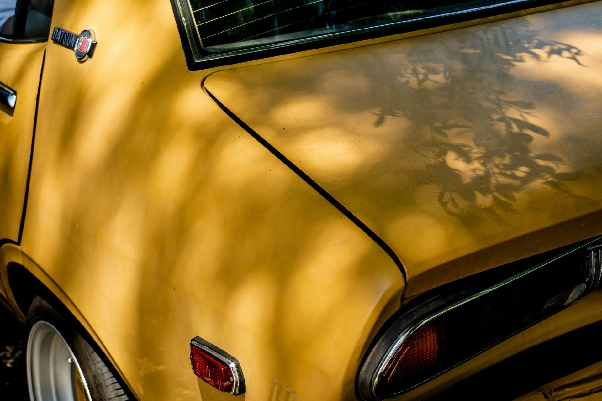 A close up of a yellow car with a tree shadow on it