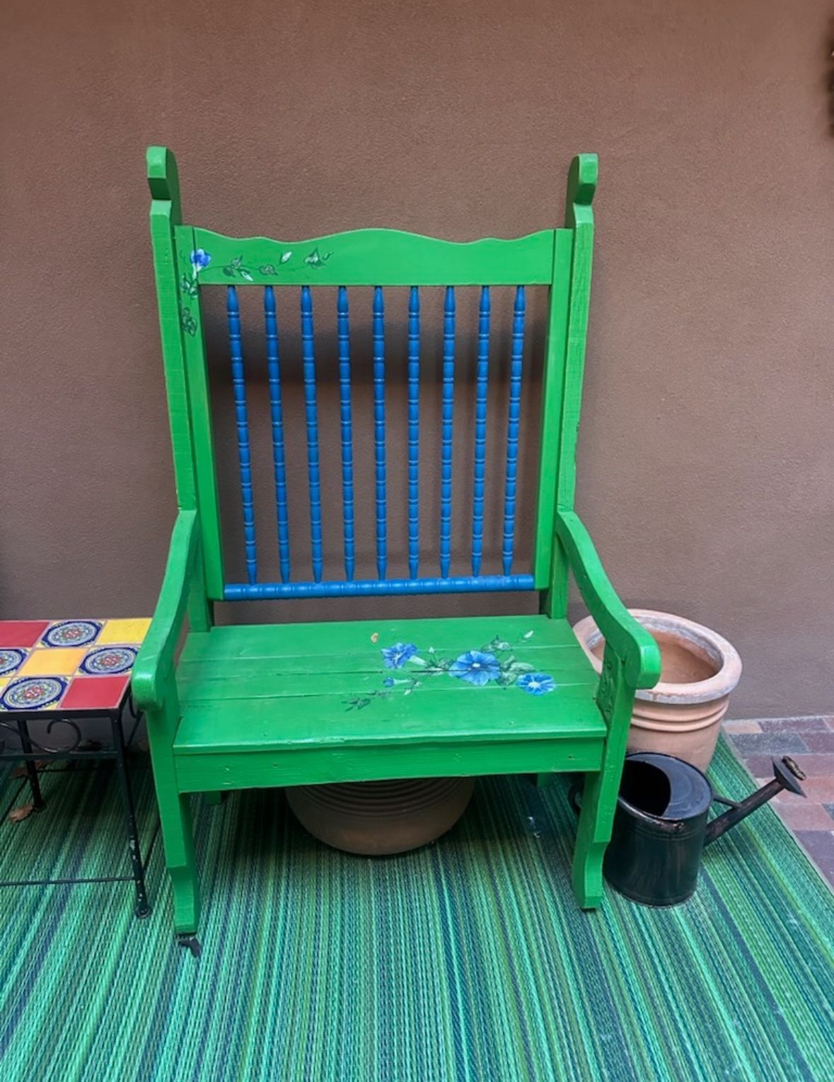A green and blue chair is sitting on a green rug next to a watering can