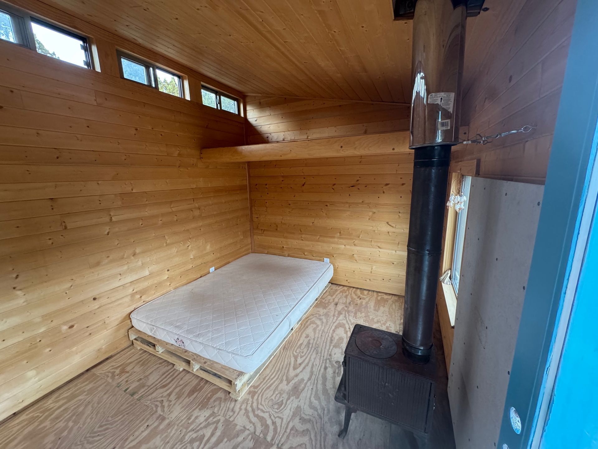 The inside of a wooden cabin with a bed and a stove.