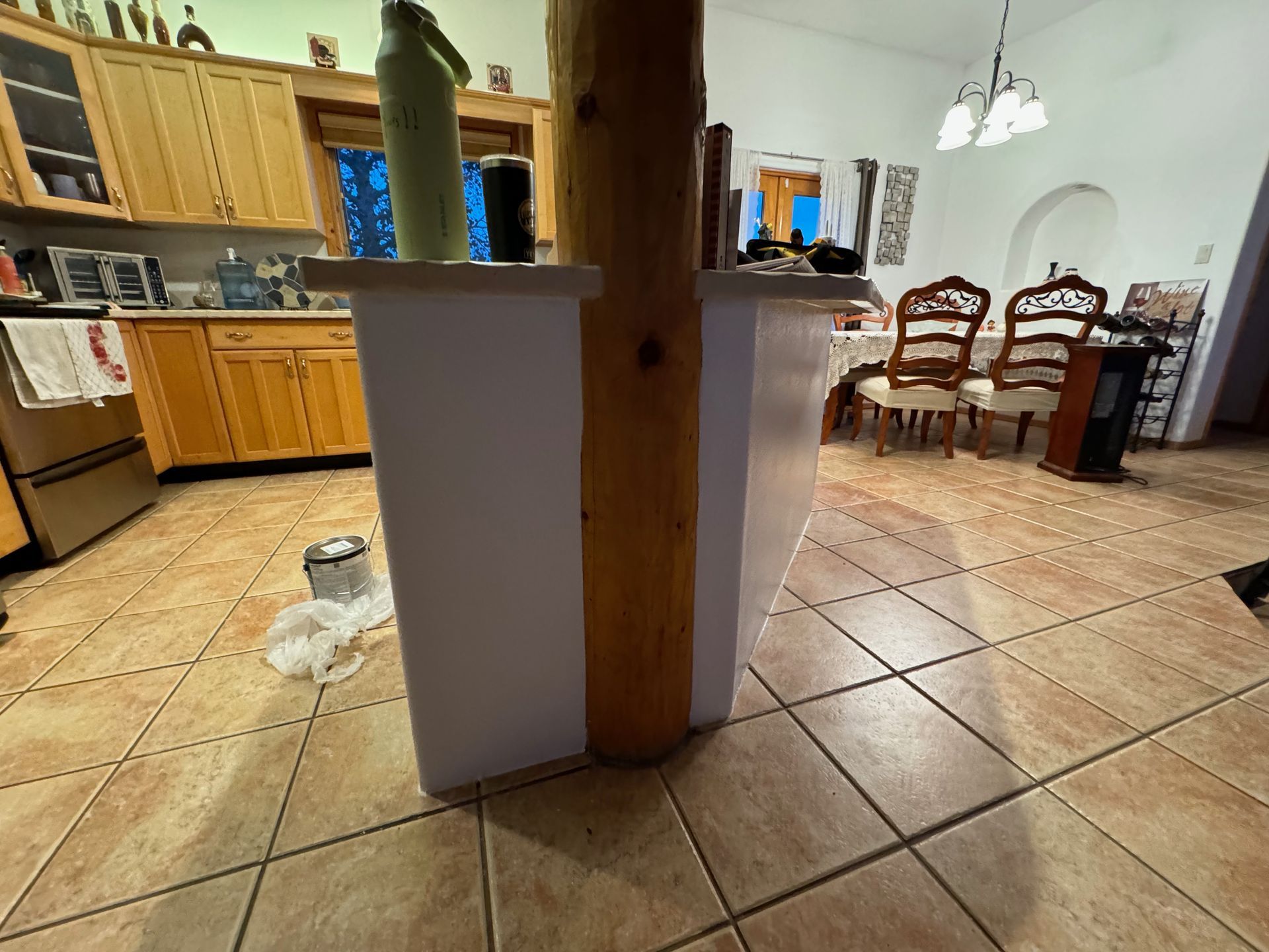 A kitchen with wooden cabinets and tile floors and a large white container in the middle of the room.