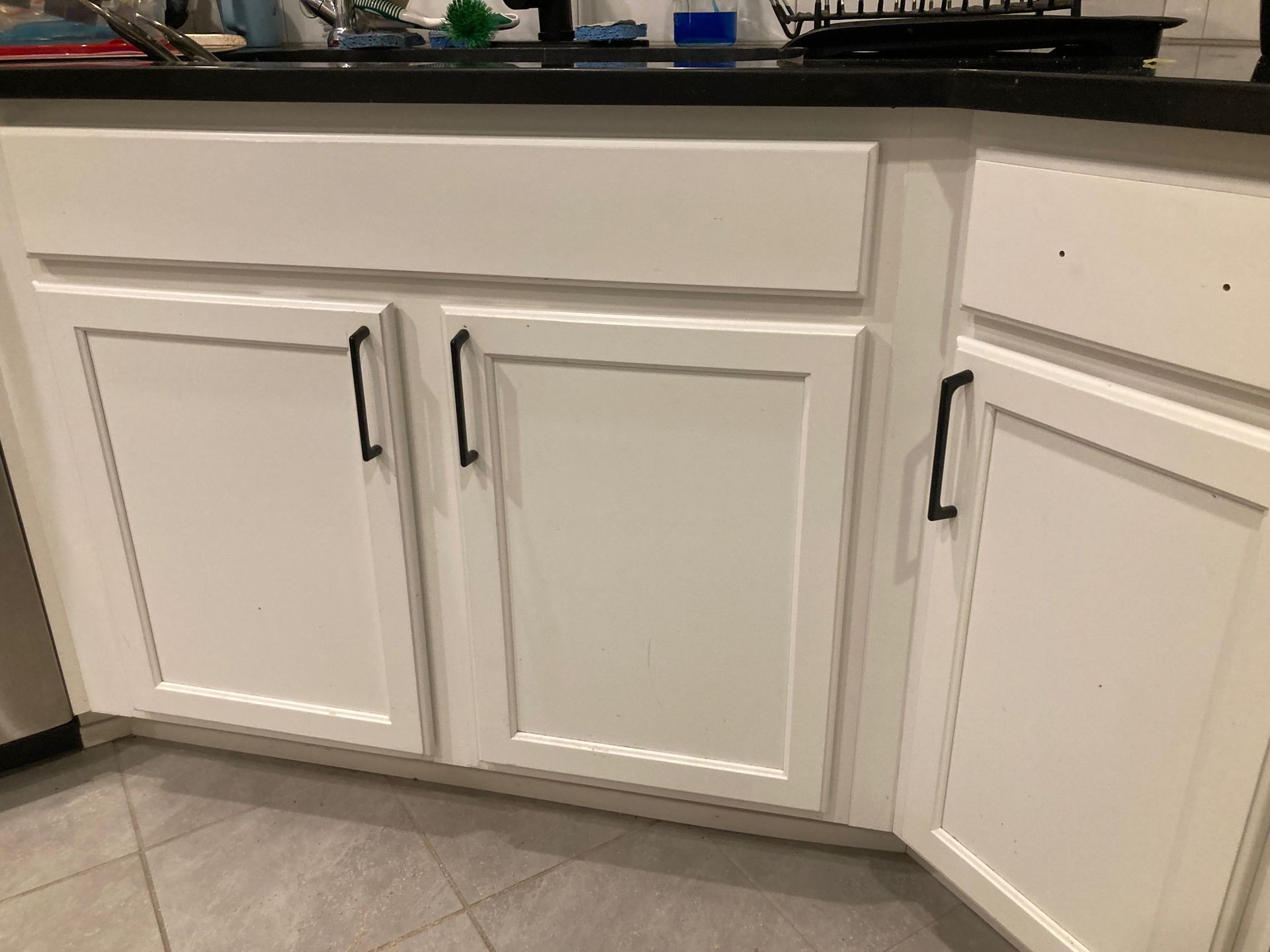 A kitchen with white cabinets and a black counter top.