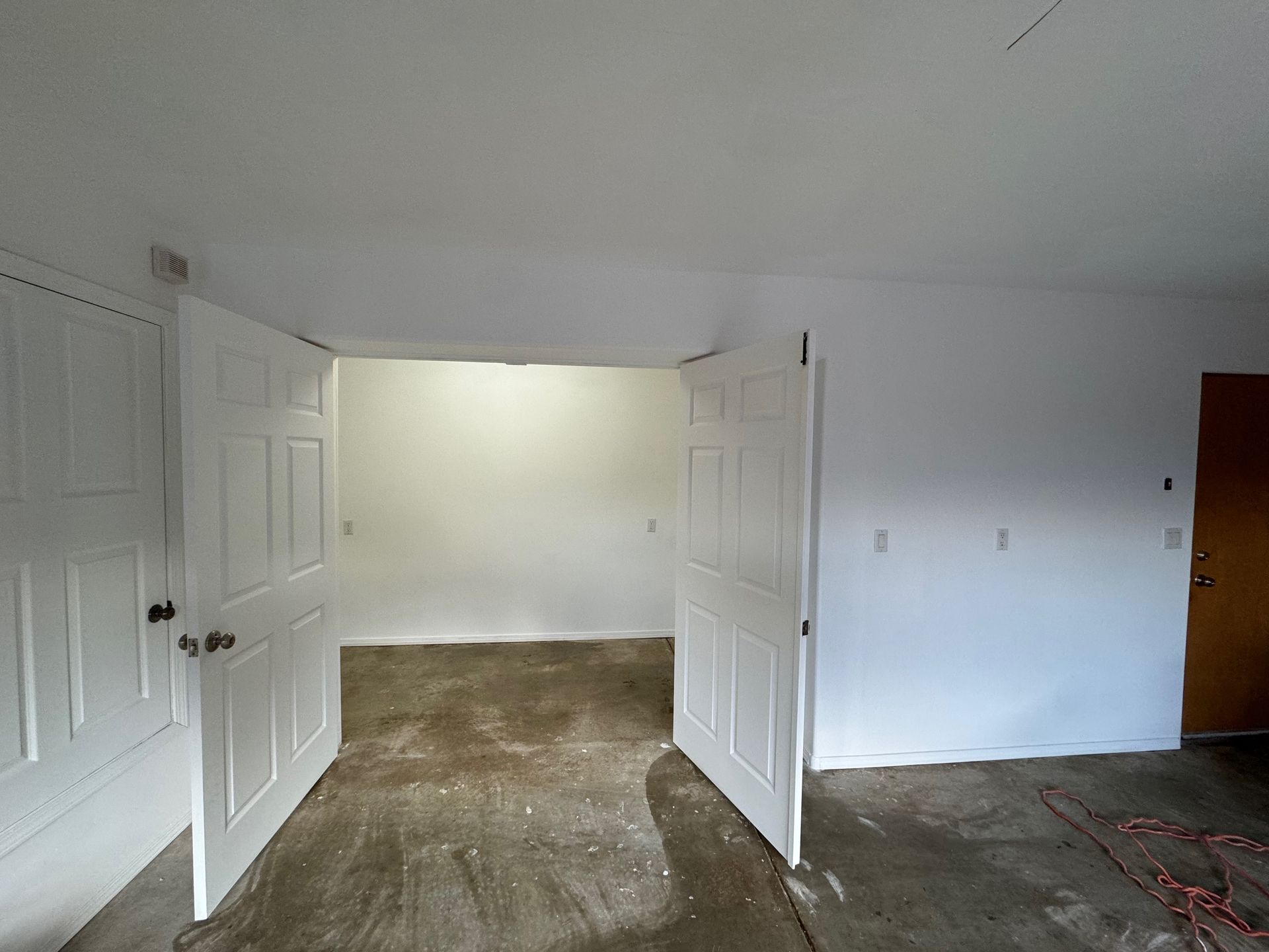 An empty room with two doors open and a carpeted floor.