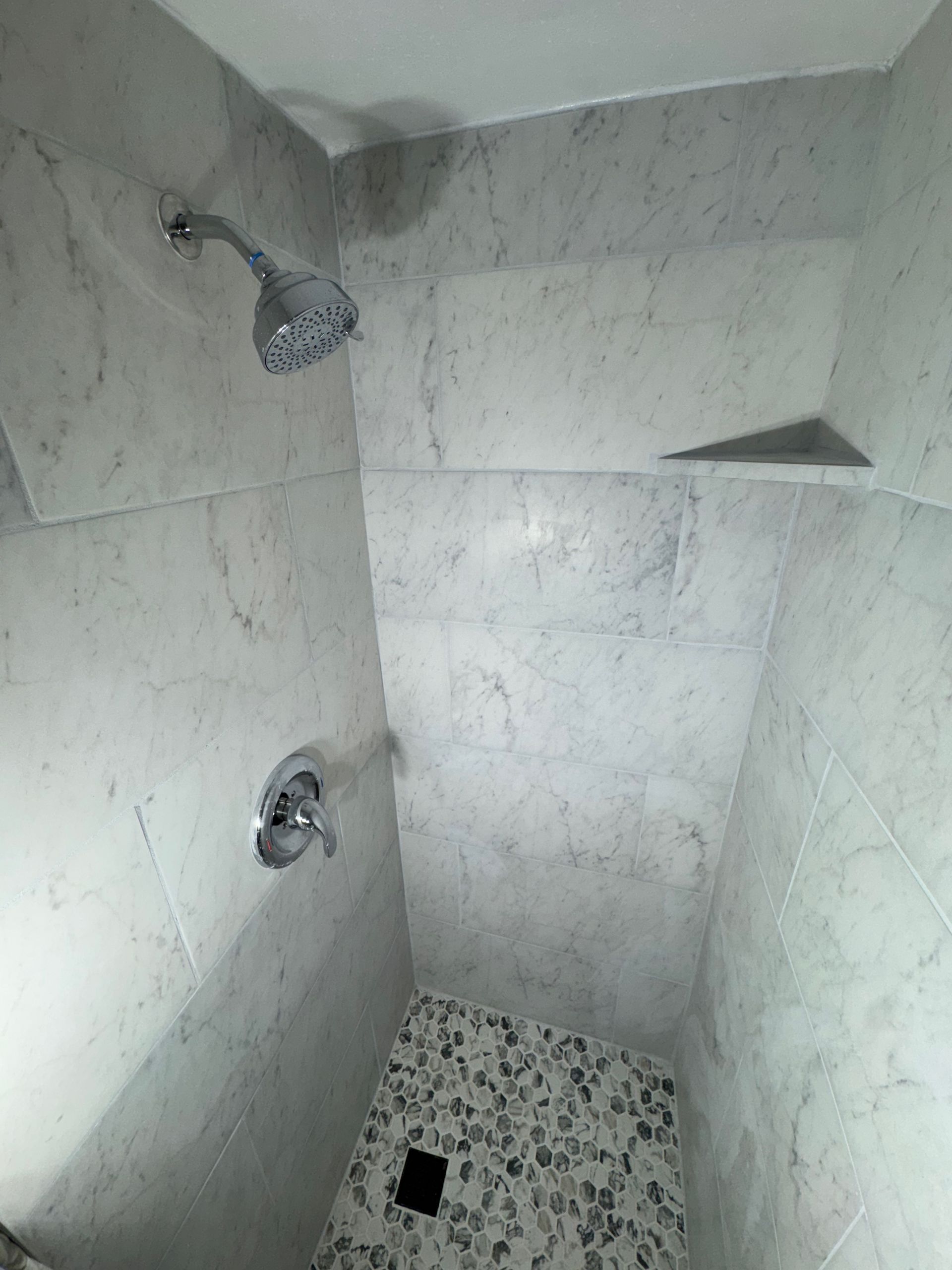 A shower with a shower head and a tiled floor in a bathroom.