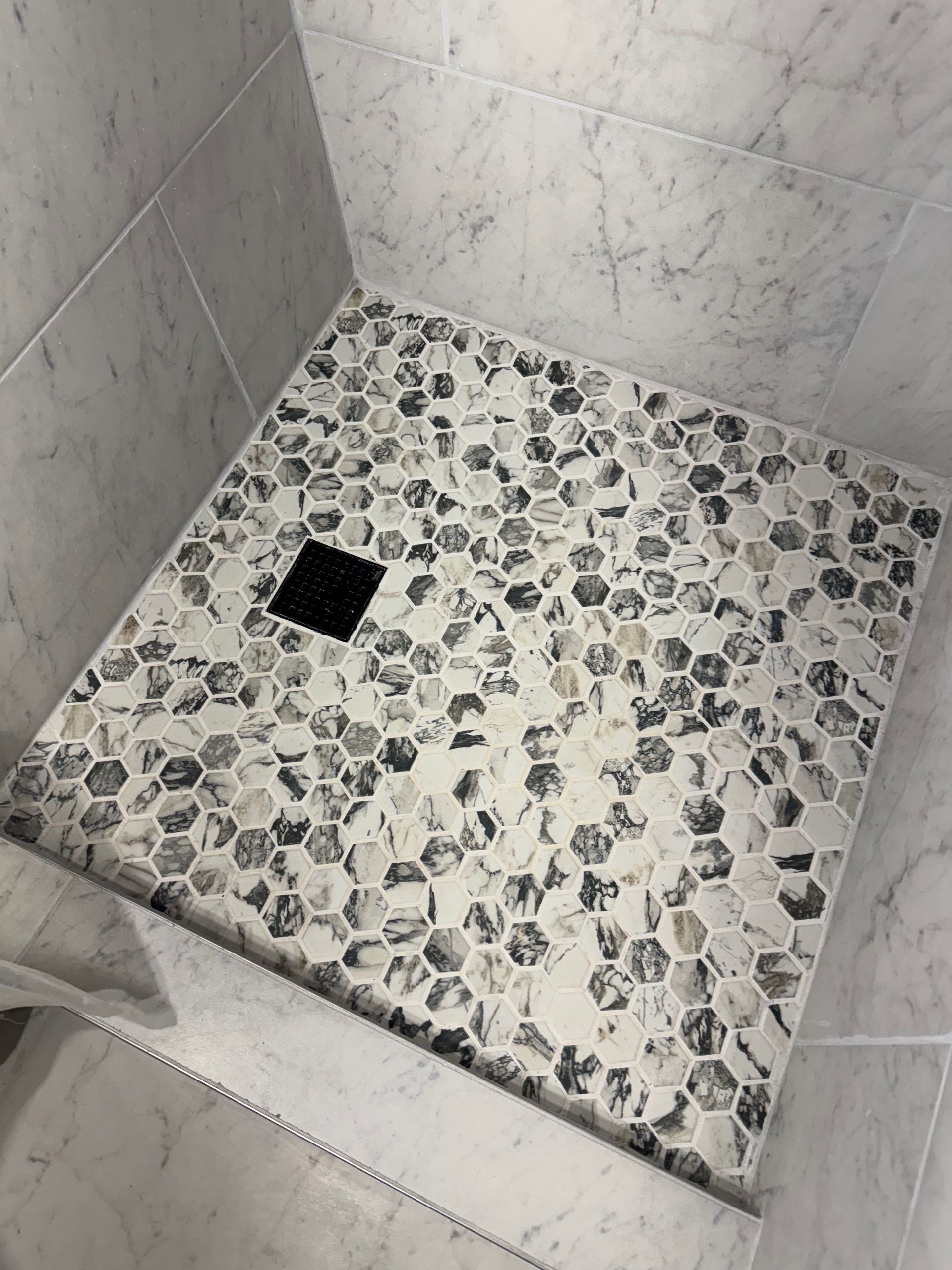 A black and white tiled shower stall with a black drain.