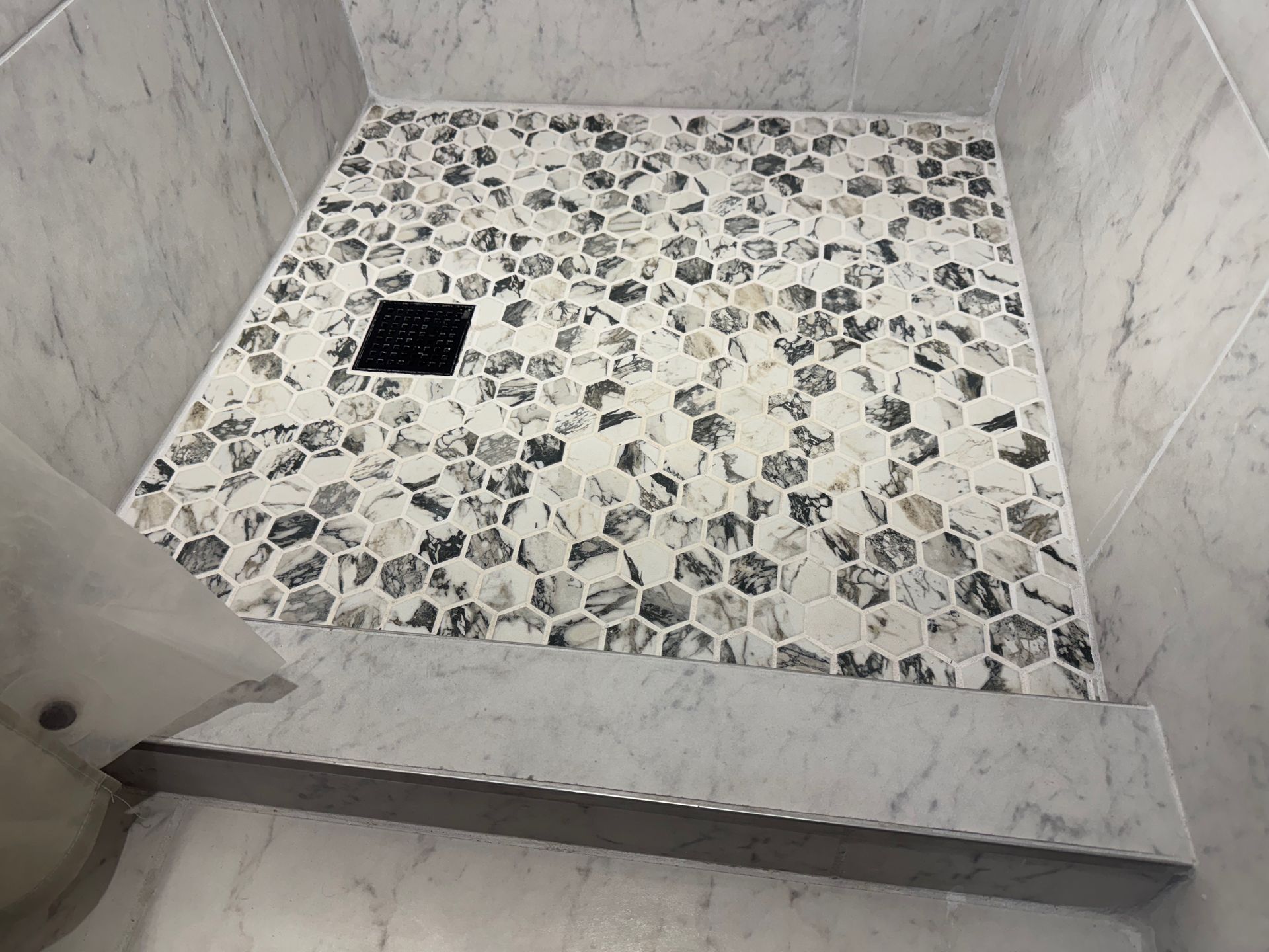A shower stall with a tiled floor and a black drain.