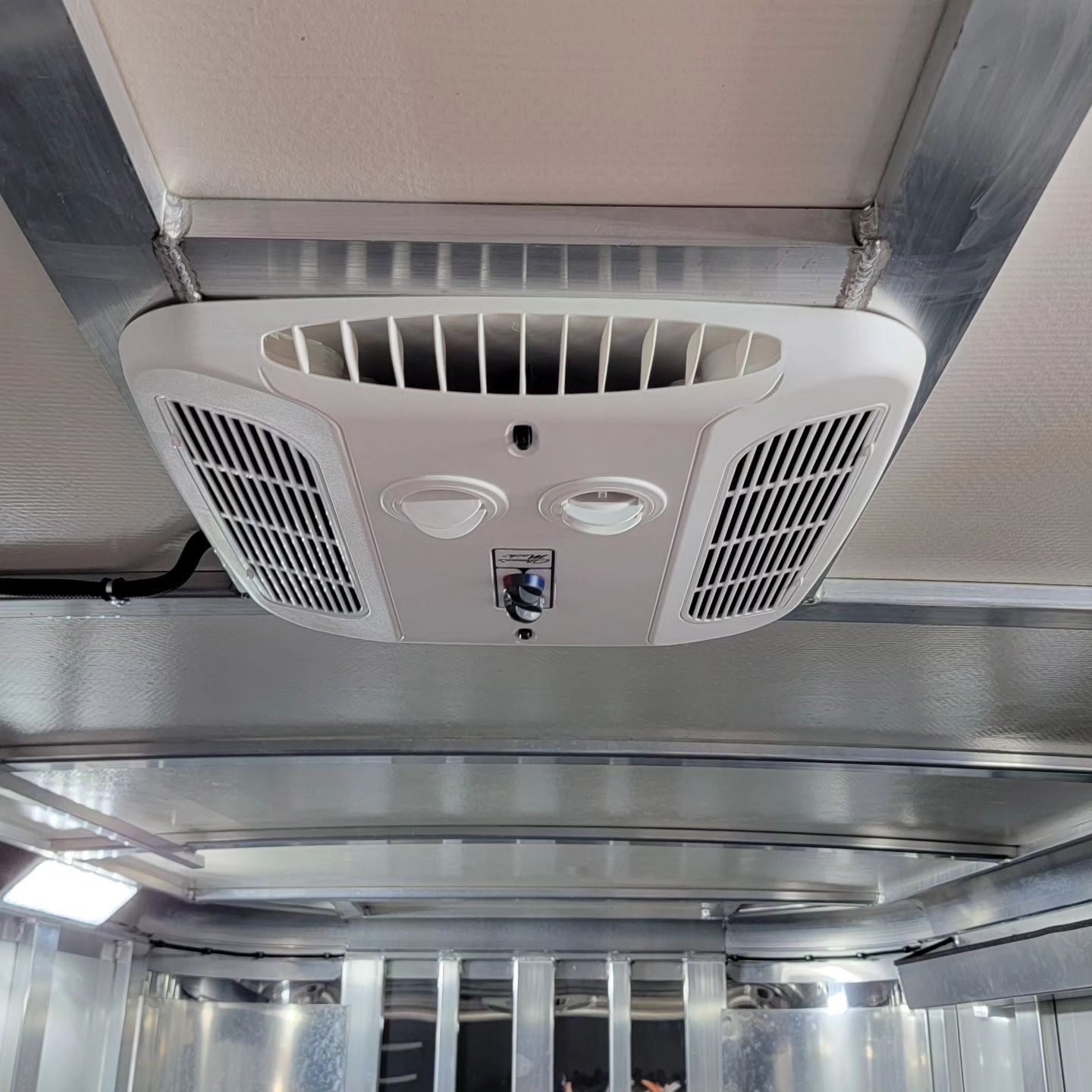 White air conditioning unit mounted in a metal trailer ceiling.
