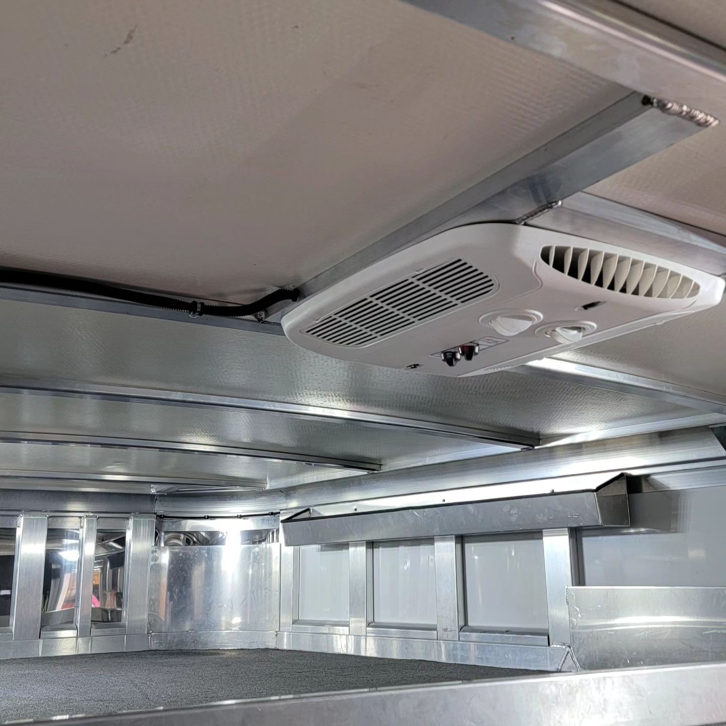 Interior view of a horse trailer ceiling with an air conditioning unit installed. Silver metal supports and white panels.