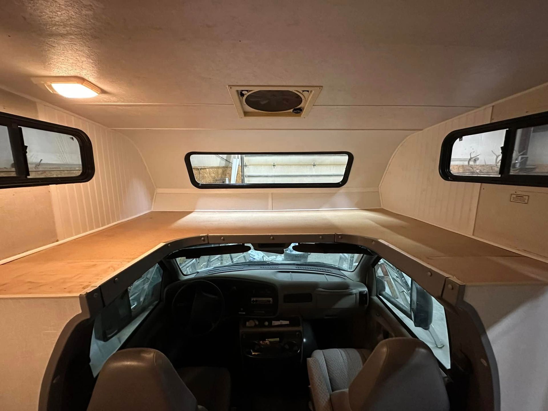 Interior of a camper, with a bed over the driver's area, windows, and white walls.