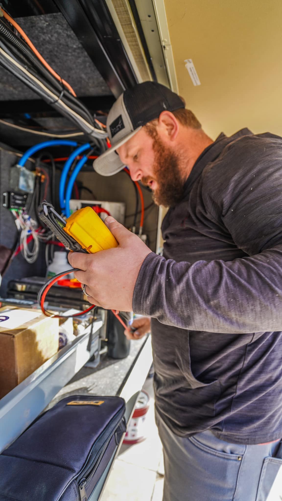 Man in cap using a multimeter on electrical components inside a vehicle, inspecting wiring.