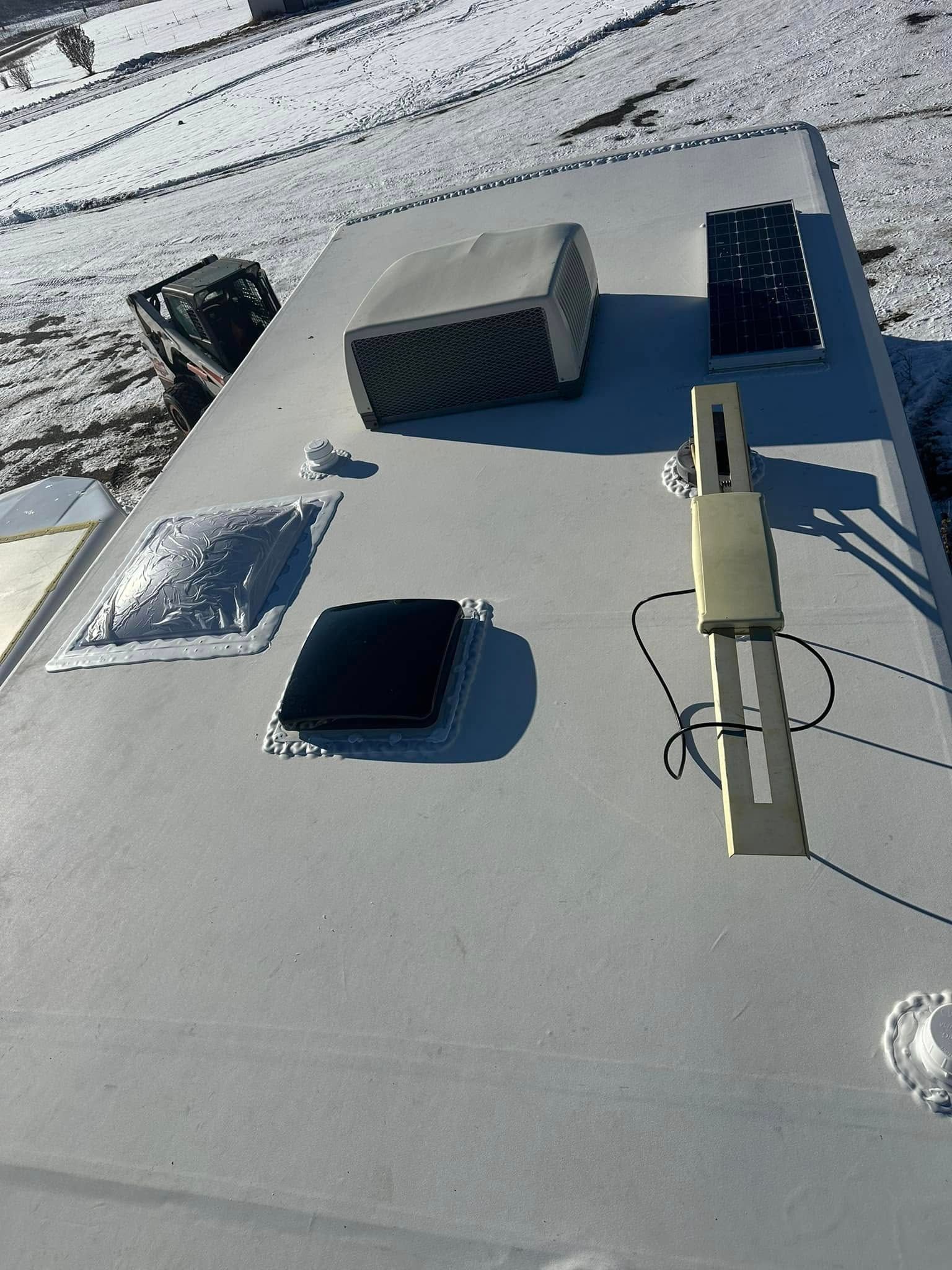 White RV roof with various vents, solar panels, and a satellite dish. Snowy background.