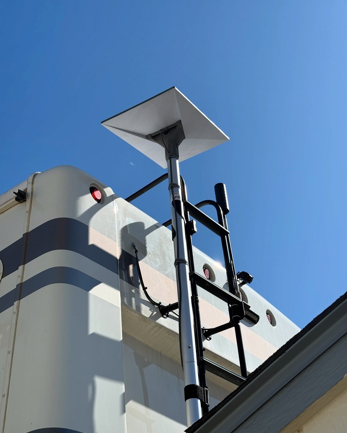 A white satellite dish mounted on a telescoping pole, attached to a RV; blue sky in background.
