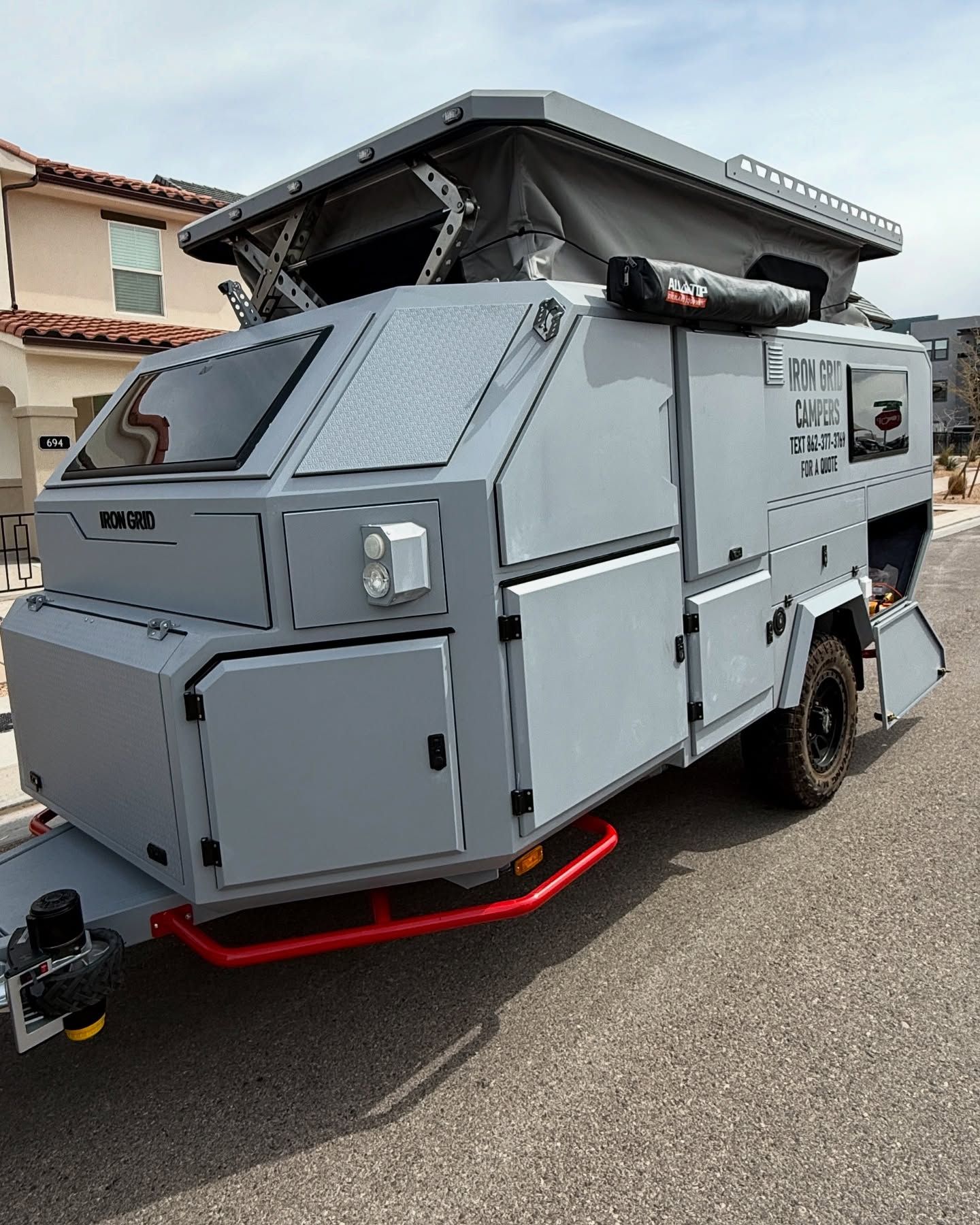 Gray, off-road camper trailer with pop-up roof parked on a paved road in front of houses.