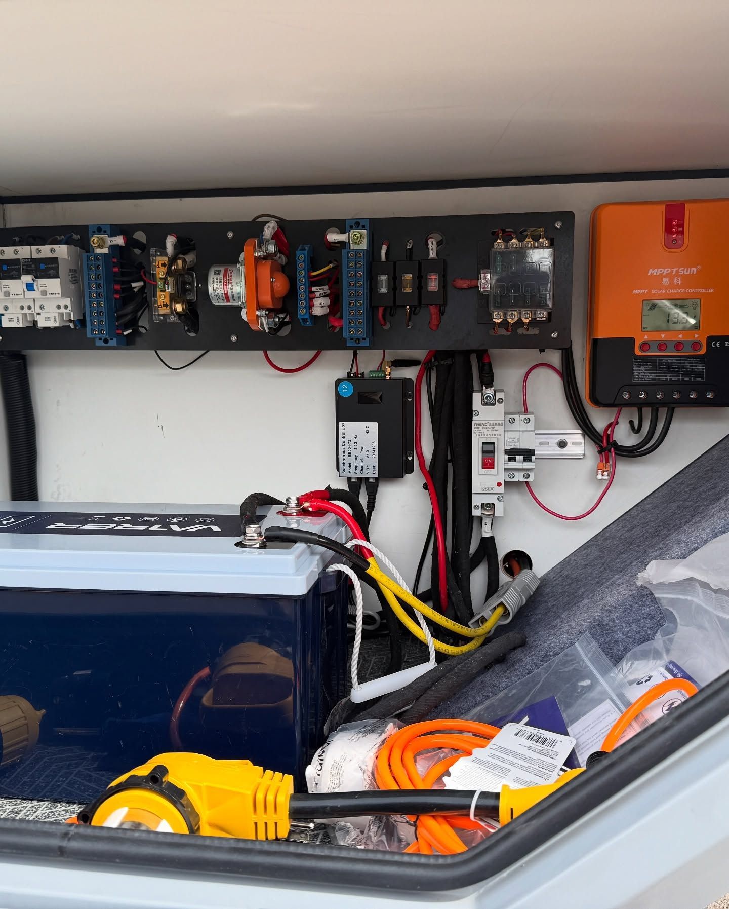Solar power system components mounted on a black panel; an orange charge controller, circuit breakers, and wiring.