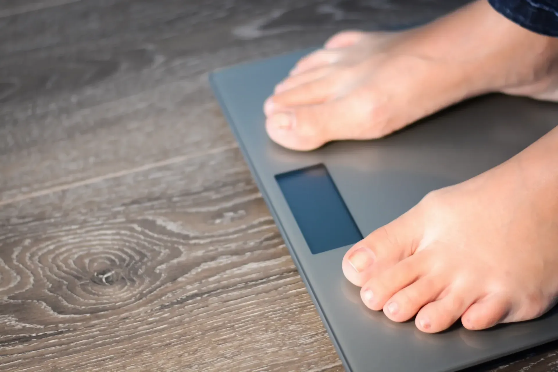 A person is standing on a scale on a wooden floor.