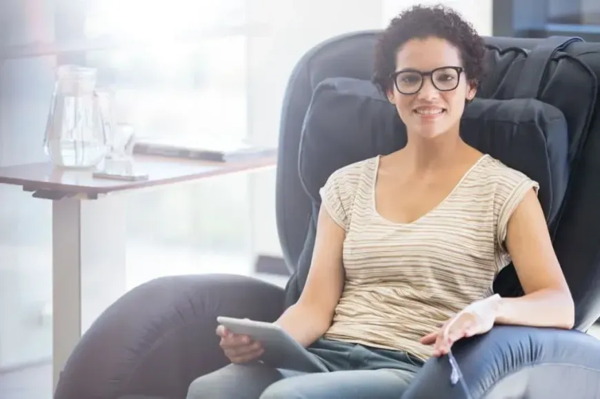 A woman is sitting in a massage chair holding a tablet.