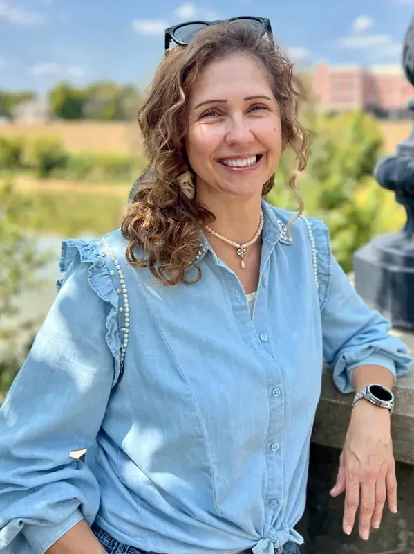 A woman wearing a denim shirt and sunglasses is smiling for the camera.