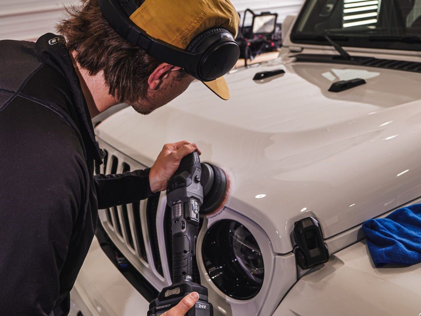 A man is cleaning a silver car with a blue cloth