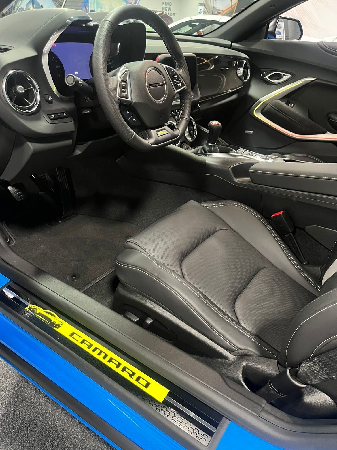 The interior of a blue and black chevrolet camaro with the door open.