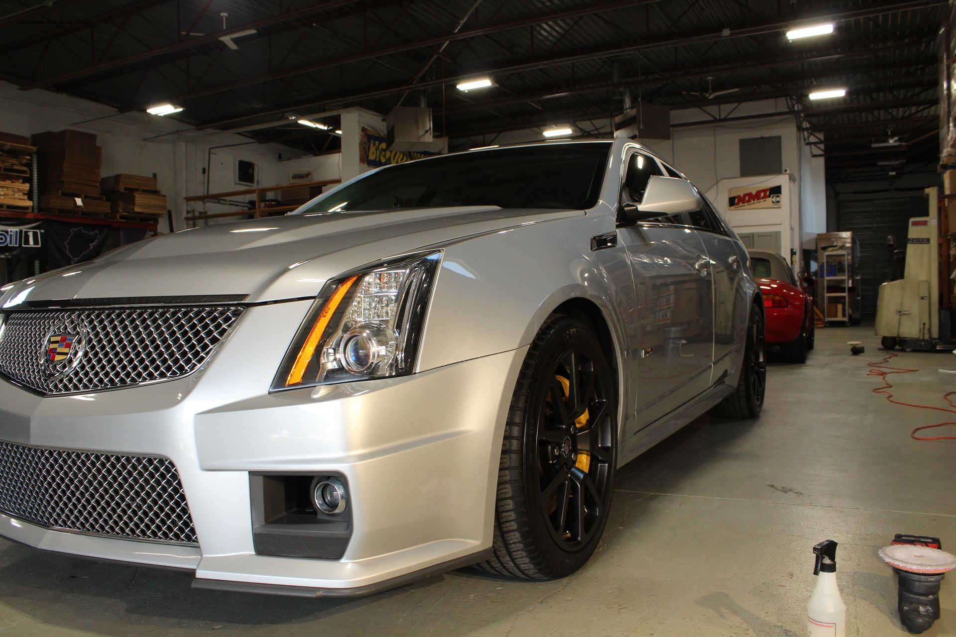 Silver Cadillac CTS-V parked in a garage, black wheels, yellow brake calipers, silver paint.
