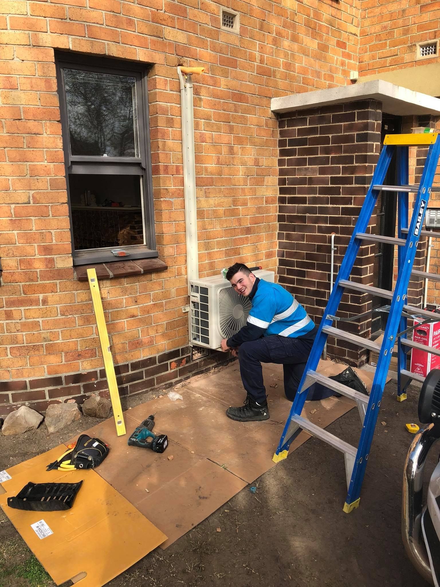 Male Electrician Checking Air Conditioner With Digital Multimeter — John B Electrical In Wooragee VIC