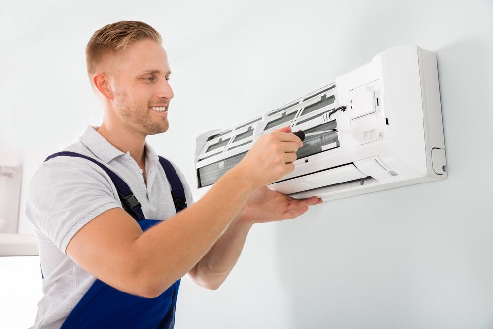 Happy Male Technician Repairing Air Conditioner With Screwdriver — John B Electrical In Yackandandah VIC