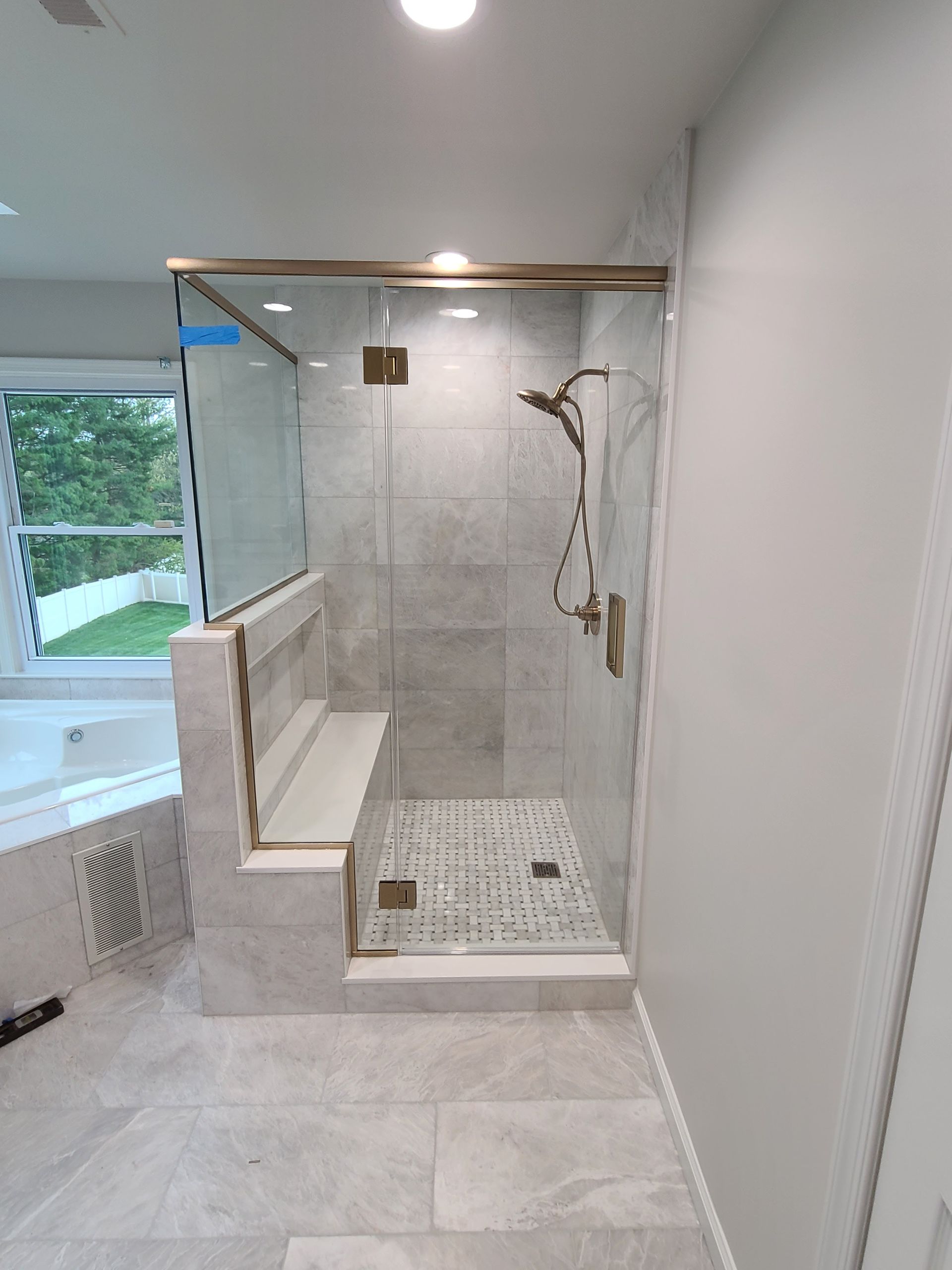 A bathroom with a walk in shower with a bench and a window.