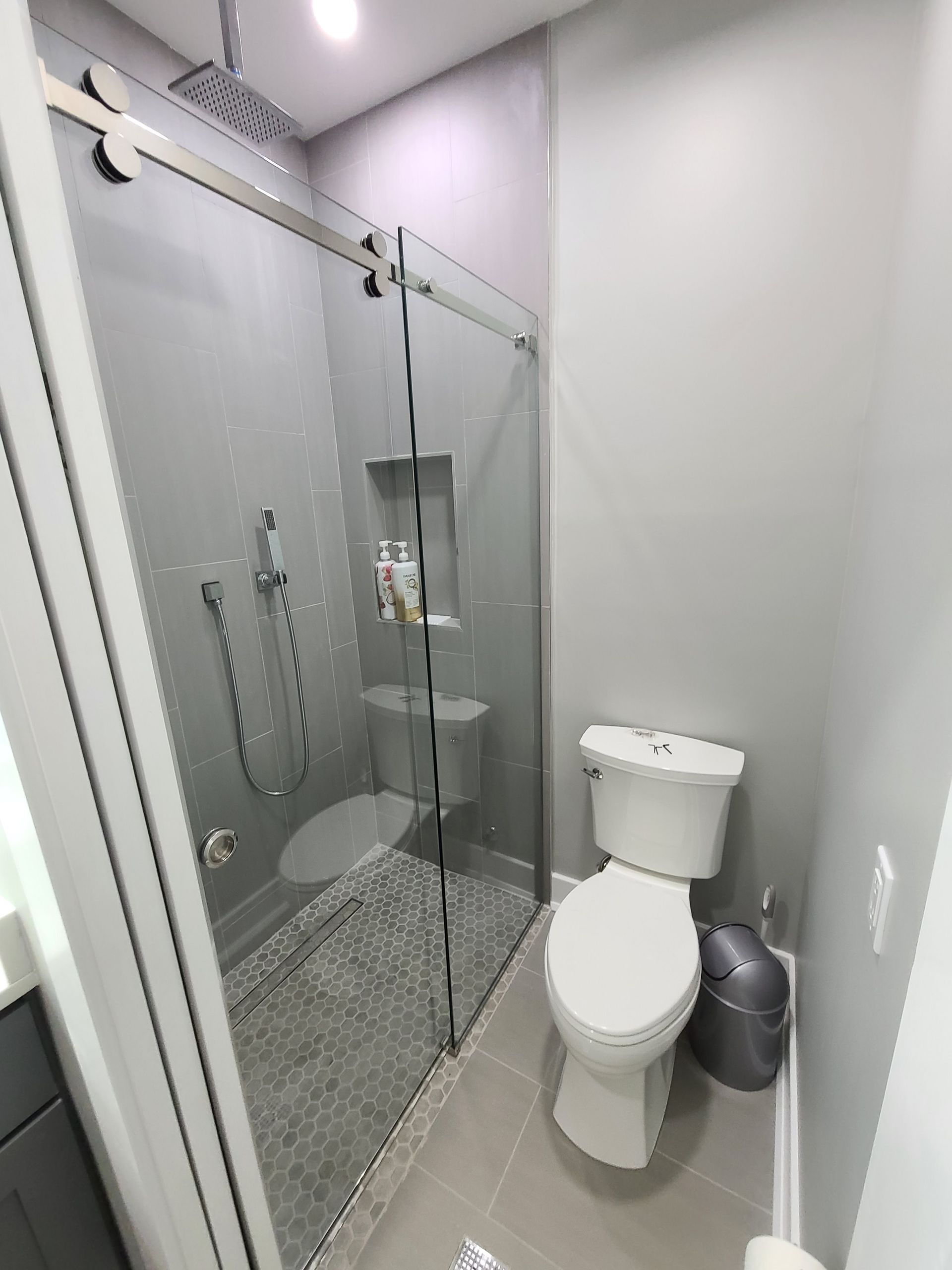 A bathroom with a toilet , shower and sliding glass door.