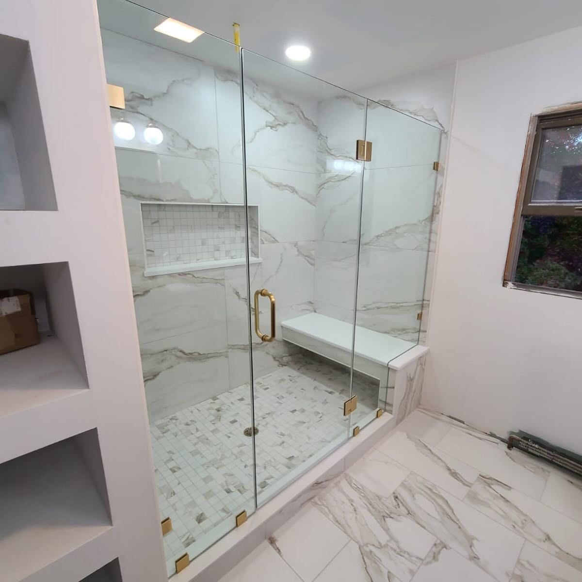 A bathroom with a glass shower door and a bench.