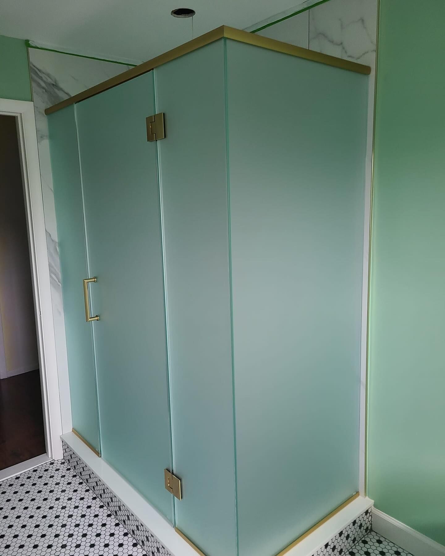 A bathroom with a shower stall with frosted glass doors and a brass frame.