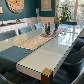 A dining room table with a glass top and a blue table runner