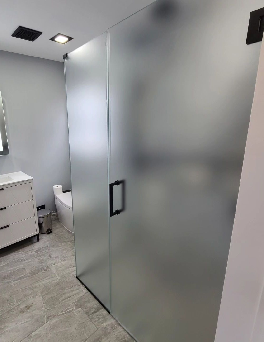 A bathroom with a toilet , sink , mirror and frosted glass shower door.