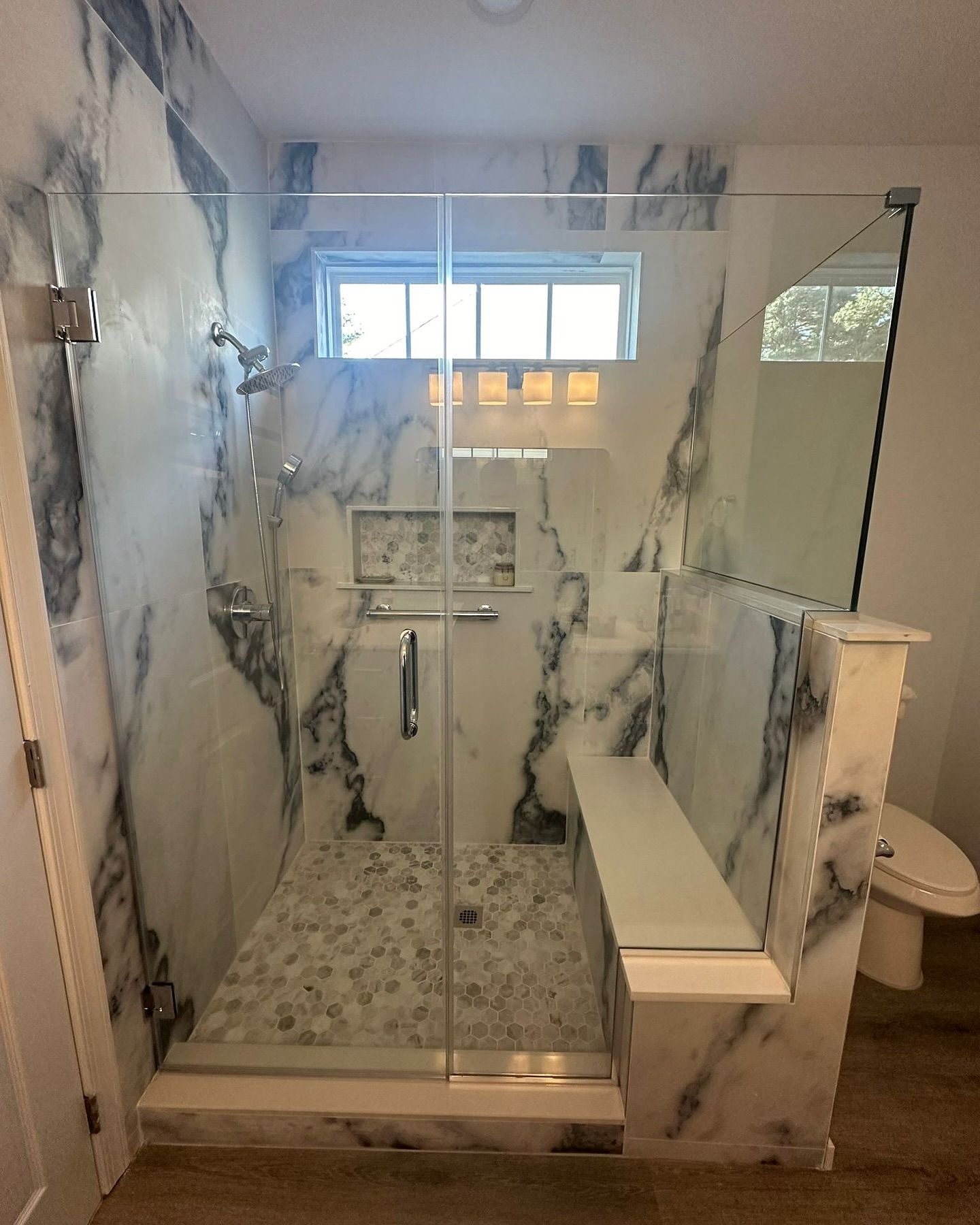 A bathroom with marble walls and a walk in shower with a glass door.
