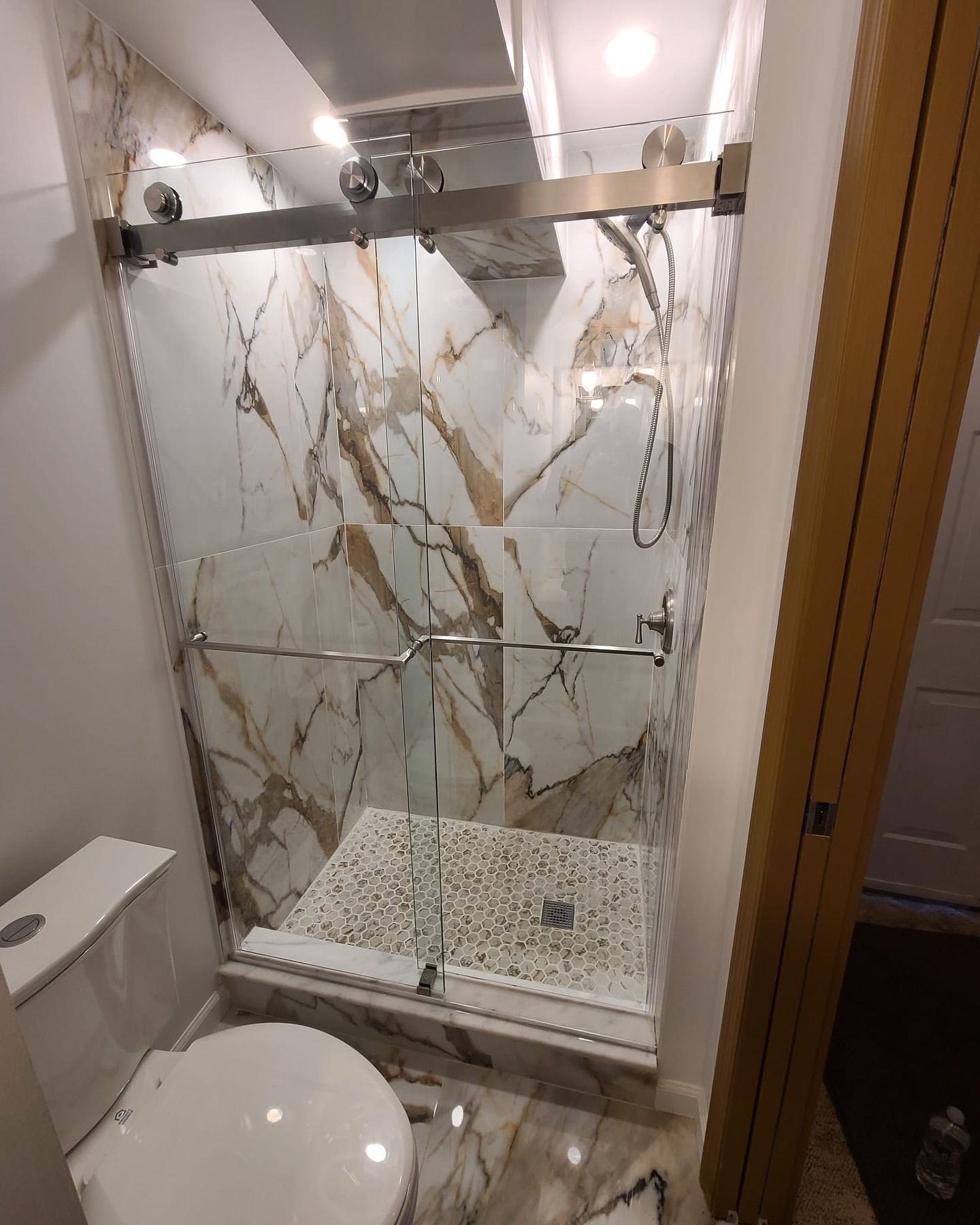 A bathroom with a toilet , shower , and marble walls.