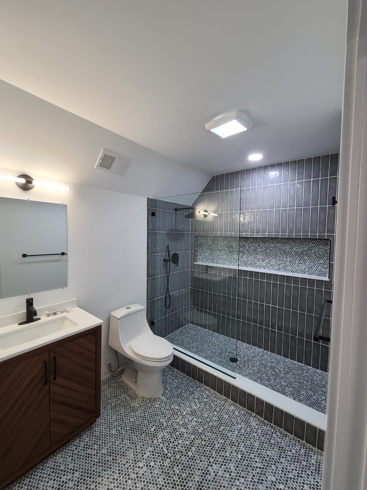 A bathroom with a toilet , sink , shower and mirror.
