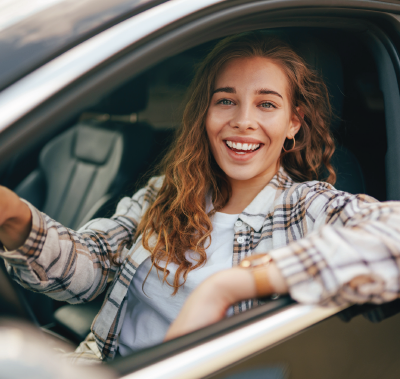 Woman smiling, sitting in car with arm resting on window, plaid shirt.