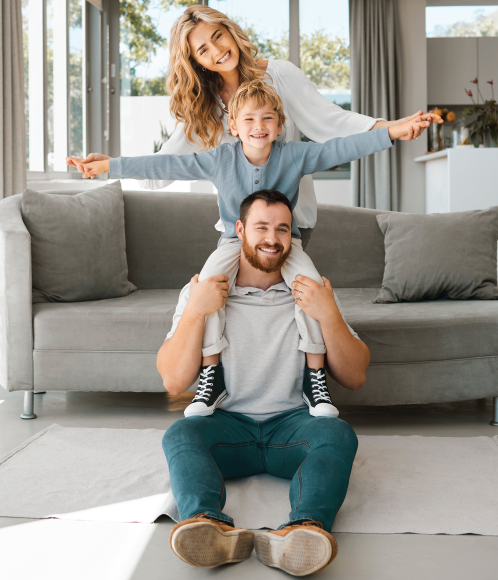 Family in living room: Child on father's shoulders, mother behind them, all smiling.