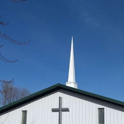 White church steeple with a cross against a bright blue sky.