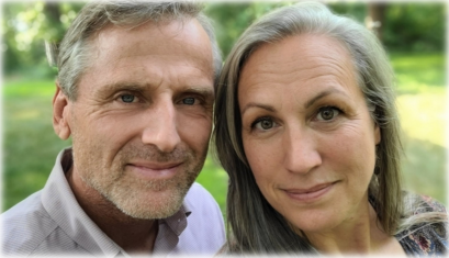 Smiling couple, man and woman, looking at the camera outdoors in a grassy area.