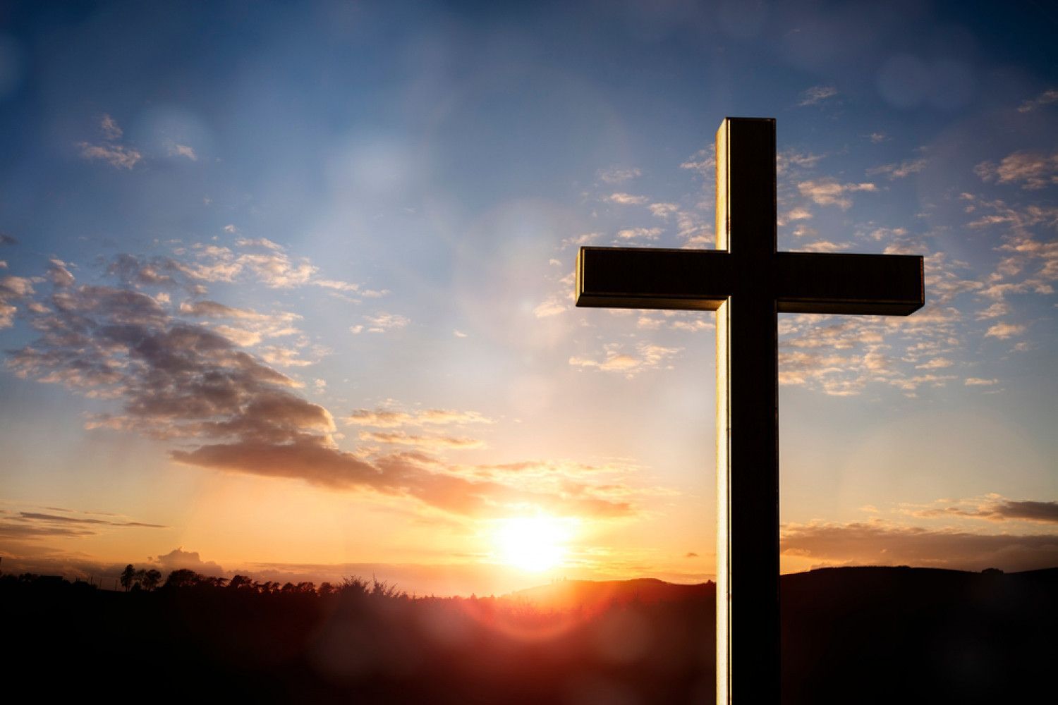 Cross silhouetted against a sunset with orange and blue sky.