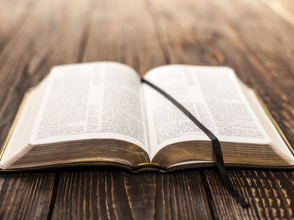 Open Bible with black ribbon bookmark on a wooden surface.