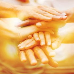 Hands stacked together in a gesture of unity and support, bathed in warm light.