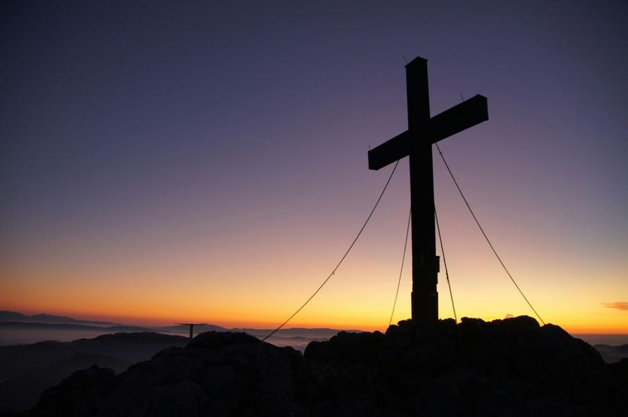 Silhouette of a cross on a mountain peak against a sunrise sky.
