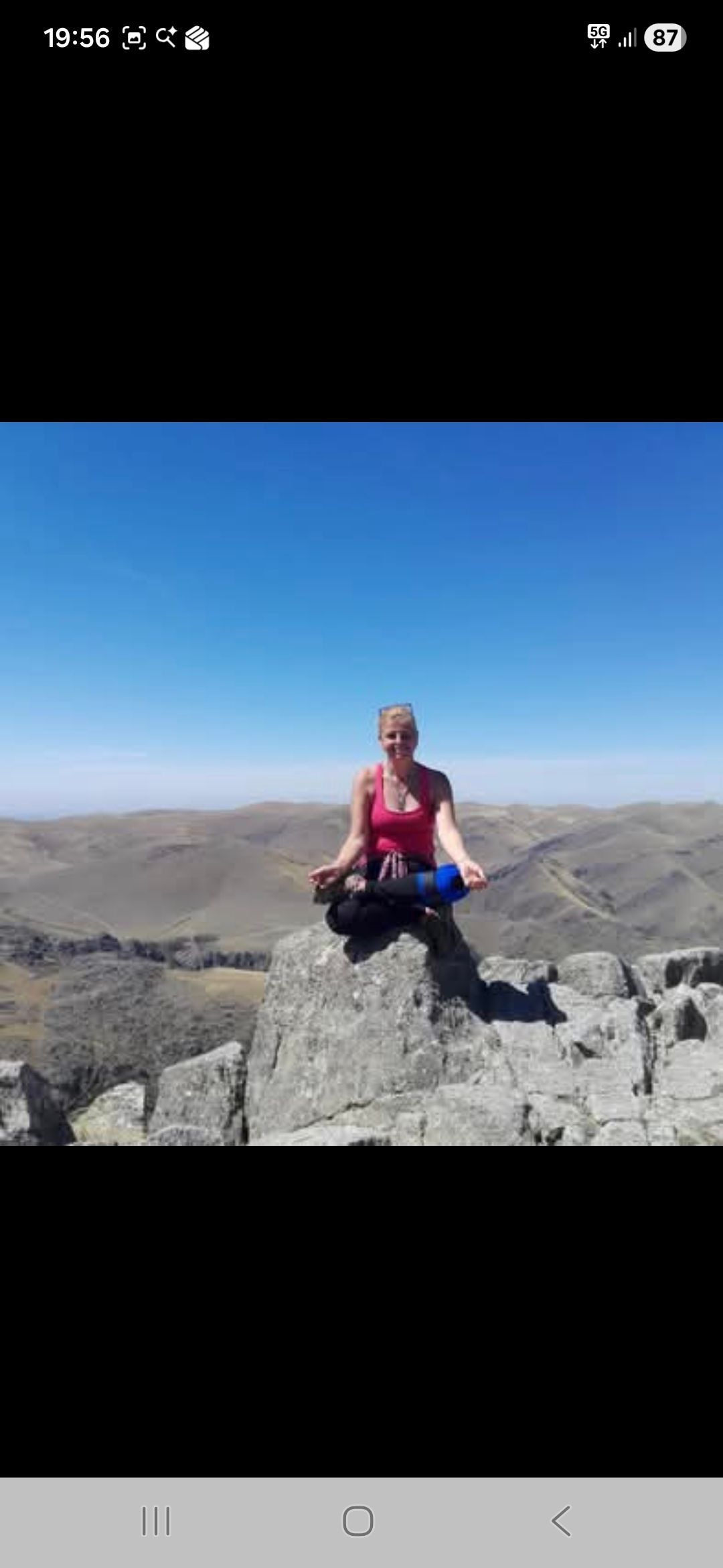 Mujer meditando en la cima de una montaña rocosa con un cielo azul claro.