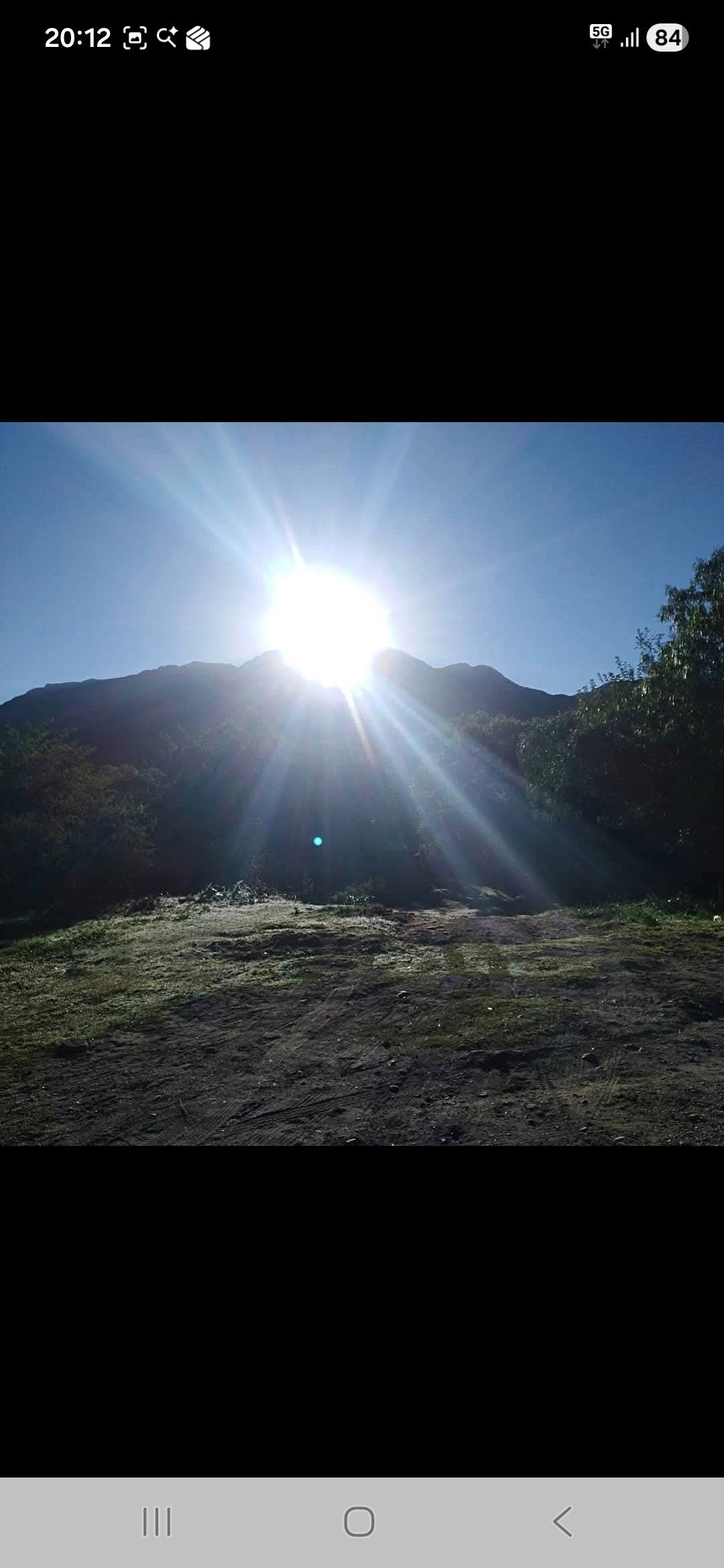 El sol brilla intensamente detrás de una montaña, recortada con vegetación oscura en primer plano.